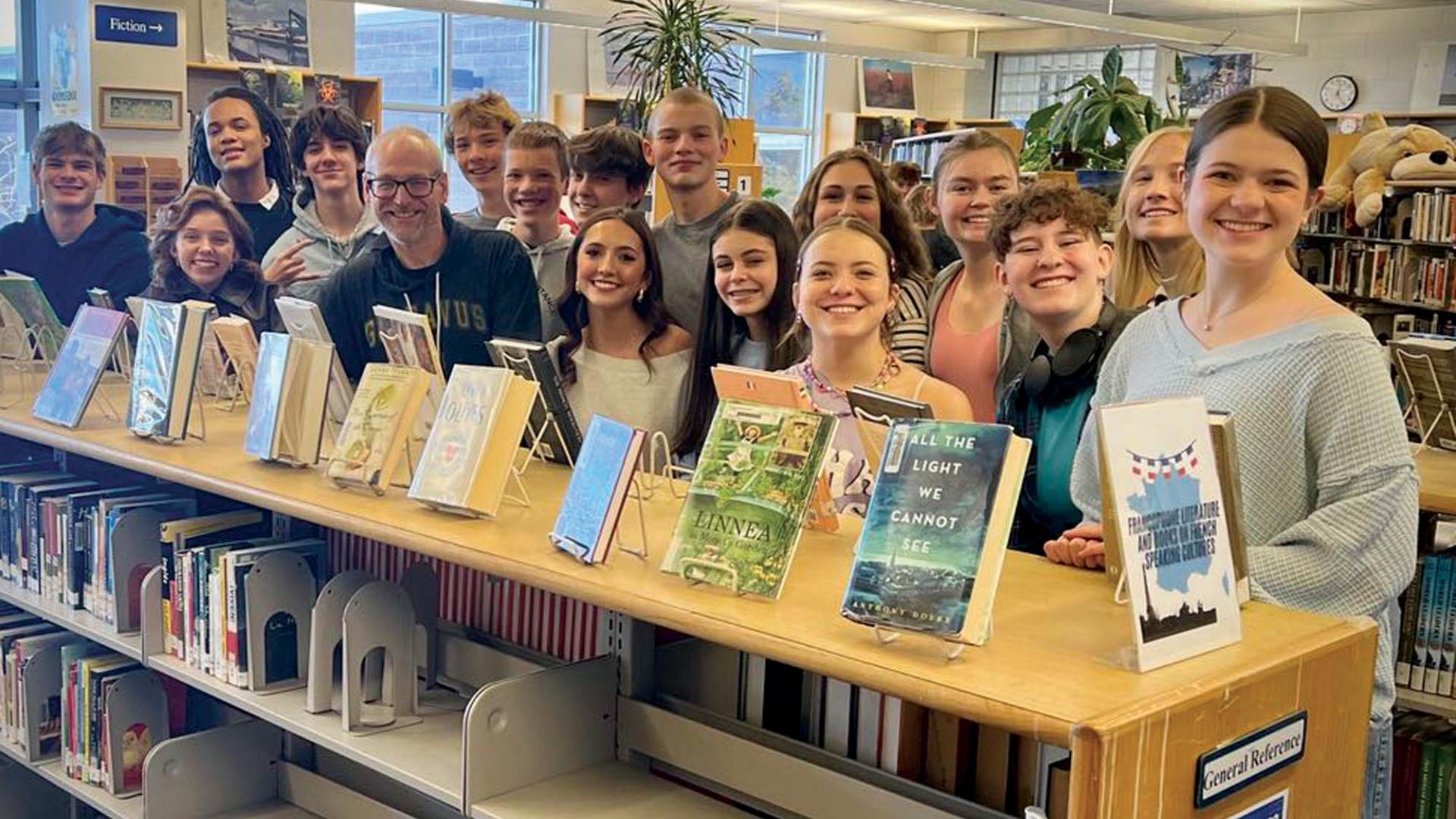 A teacher and his many middle school students in a school library. 