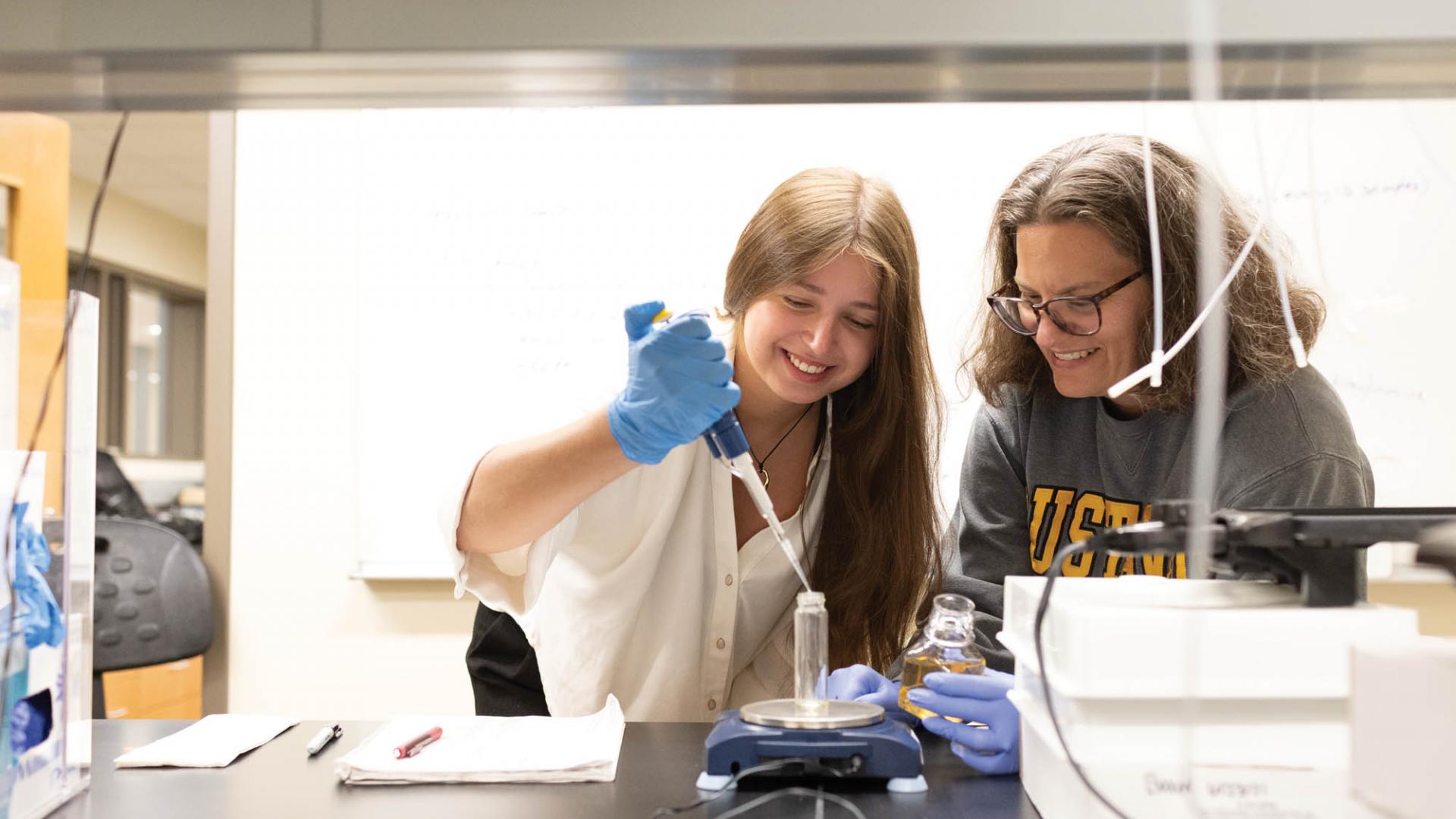 A student and a professor work with a pipette in a lab. 