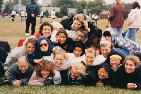 Pilar Stier in the center of all the rugby team mates at gustavus adolphus college, They are in a large pile with everyone looking at the camera. 