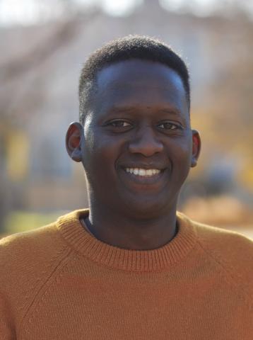 A young man in a warm golden sweater smiles for the camera.