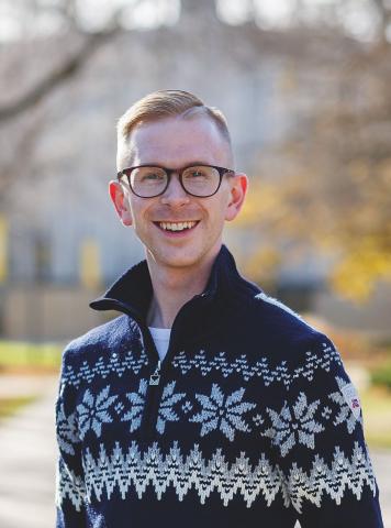 A young adult man in a Nordic sweater smiles for the camera. 
