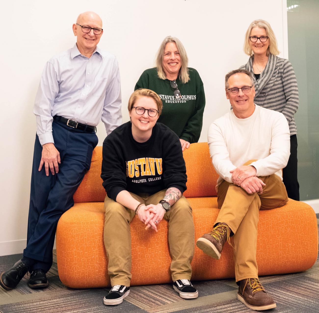 Five faculty and staff first-generation college students sit together on an orange couch