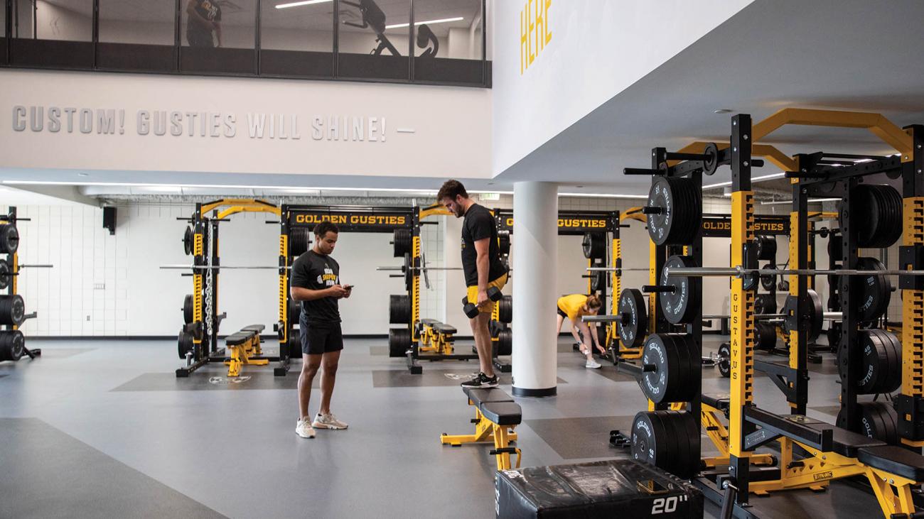 Students hanging out in a new weight room with black and gold equipment. 