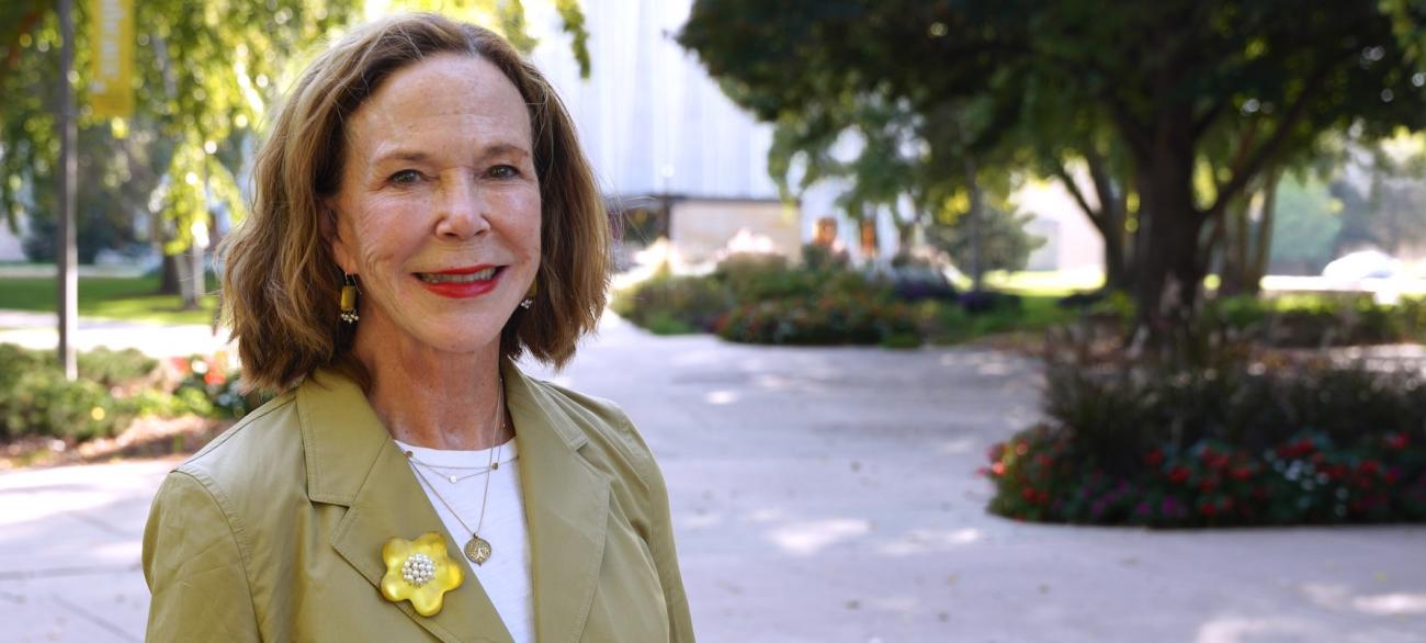 A distinguished woman stands in front of a park-like setting.