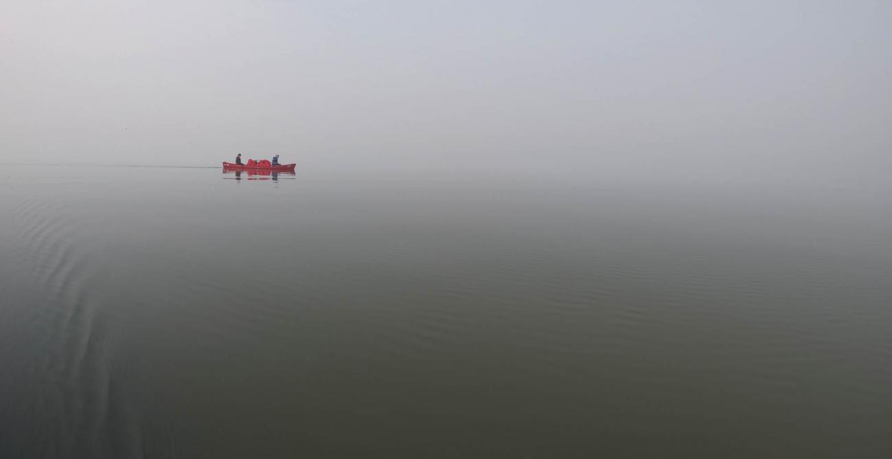 A canoe with two canoe-ers in the distance on a foggy lake day.