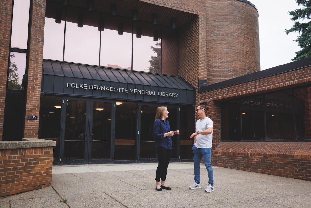 Two professors standing outside of a college library.