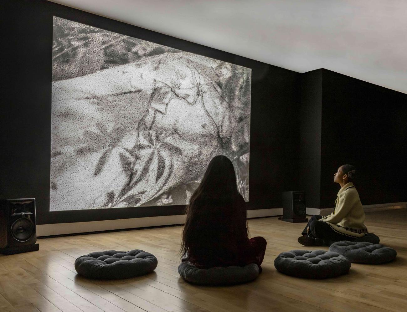 Two people sitting on floor pillows looking at black and white artwork