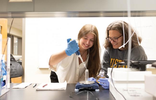 A student and a professor work with a pipette in a lab. 