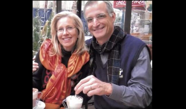 A distinguished man and woman smile for the camera while sitting at an outdoor cafe.