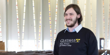 A young man with a beard and a Gustavus college sweatshirt in a chapel.