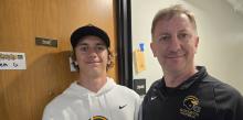 A father and son stand outside a dorm room door. 