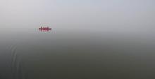 A canoe with two canoe-ers in the distance on a foggy lake day.
