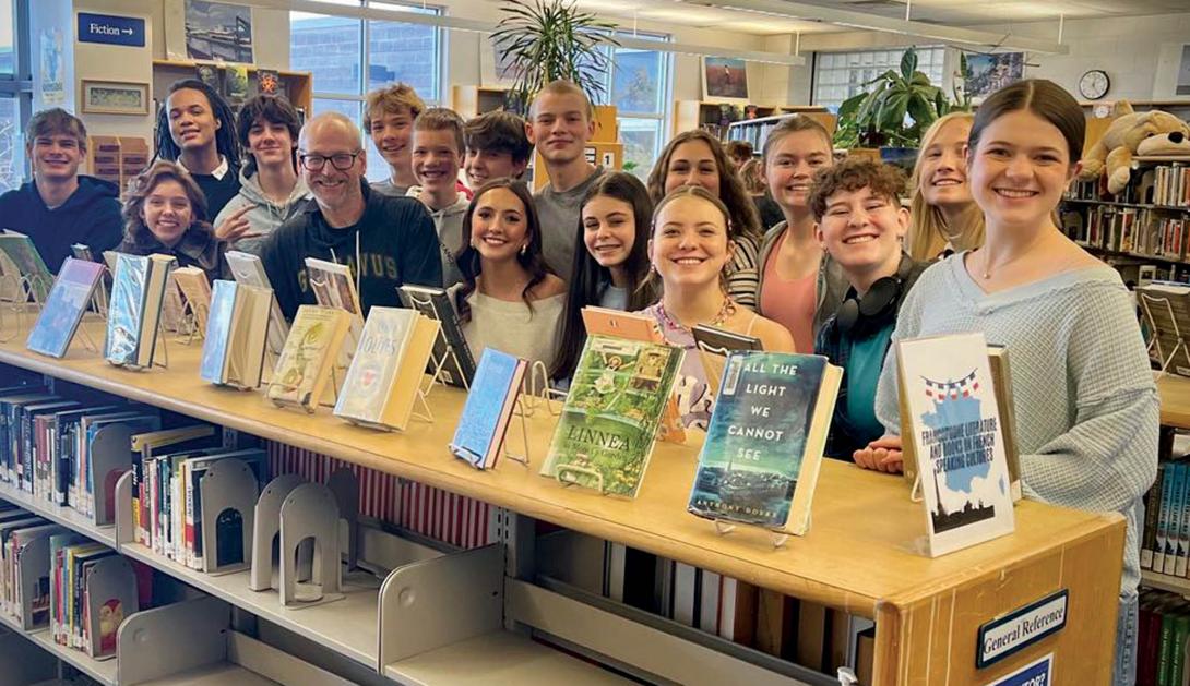 A teacher and his many middle school students in a school library. 