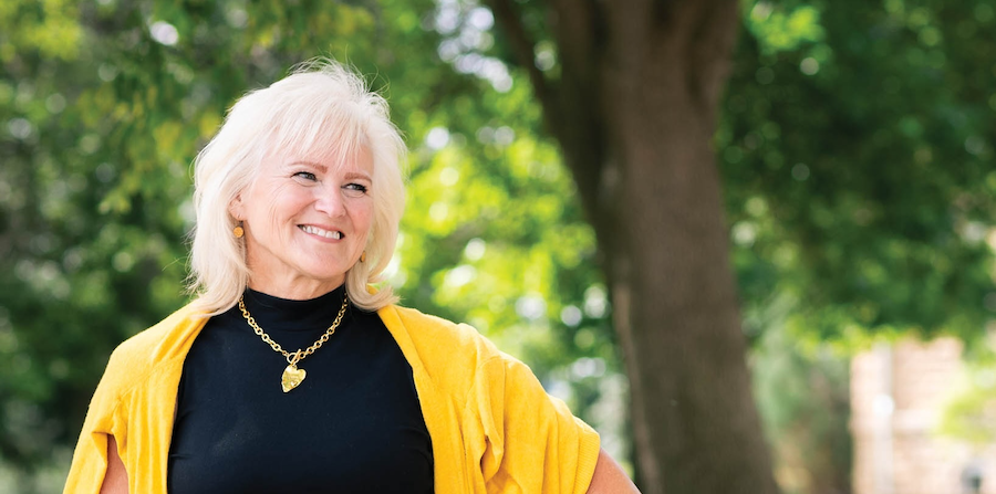 A smiling mature woman with white hair and a vibrant yellow sweater. 