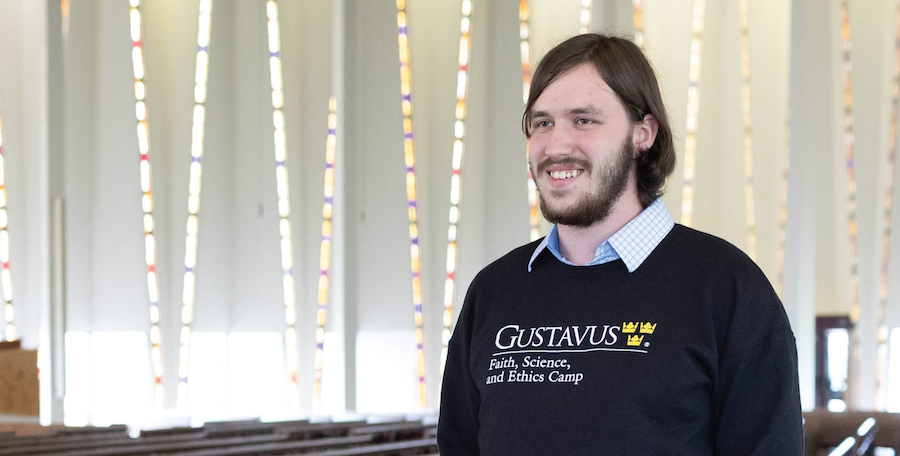 A young man with a beard and a Gustavus college sweatshirt in a chapel.