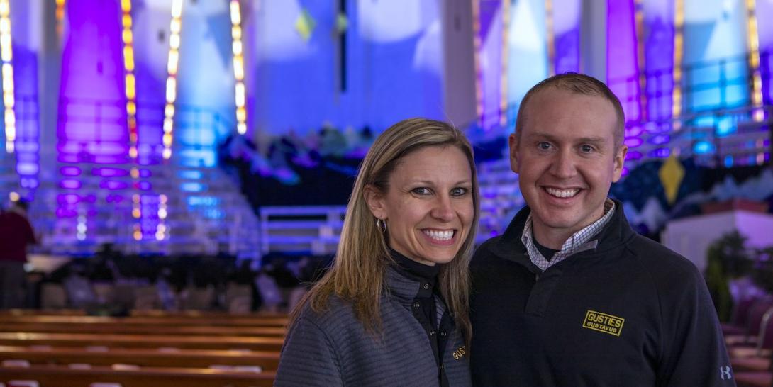 A man and a woman stand next to each other in a dramatically lit church. 