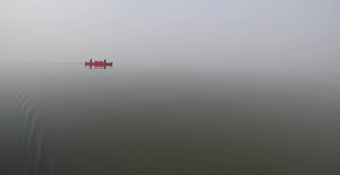 A canoe with two canoe-ers in the distance on a foggy lake day.