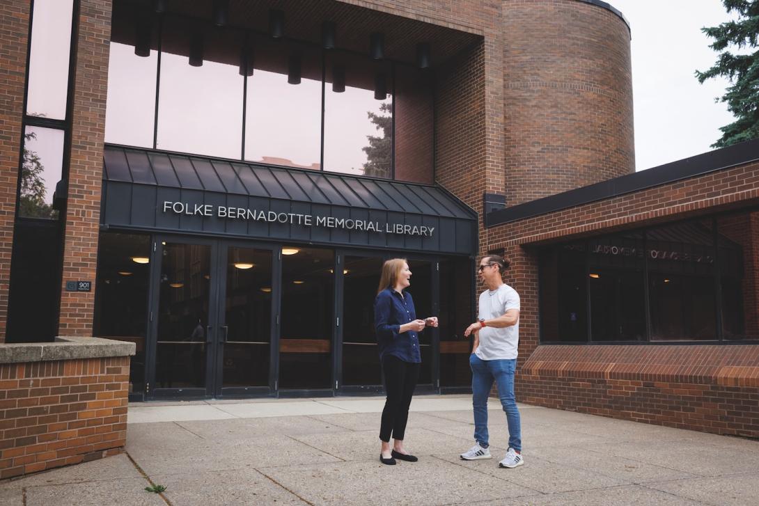 Two professors standing outside of a college library.